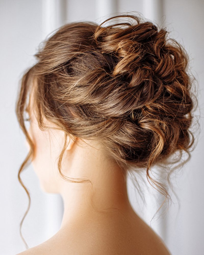 Back view of a woman with a loose, textured updo and soft tendrils at the neck.