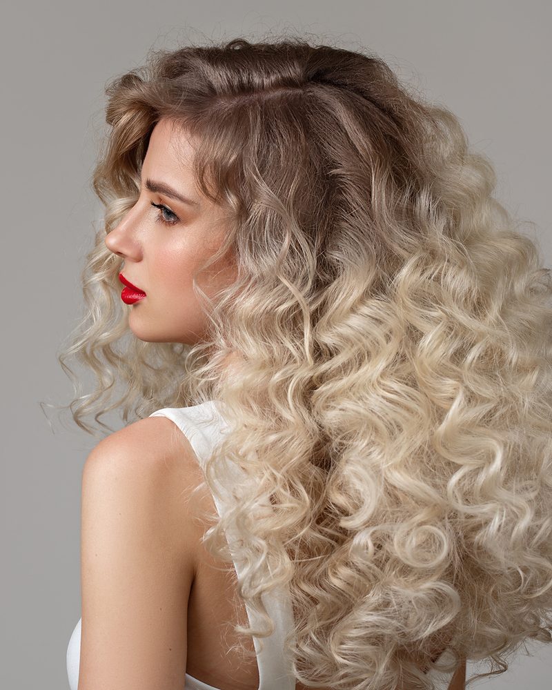 Woman with voluminous, bouncy blonde curls, seen in profile.