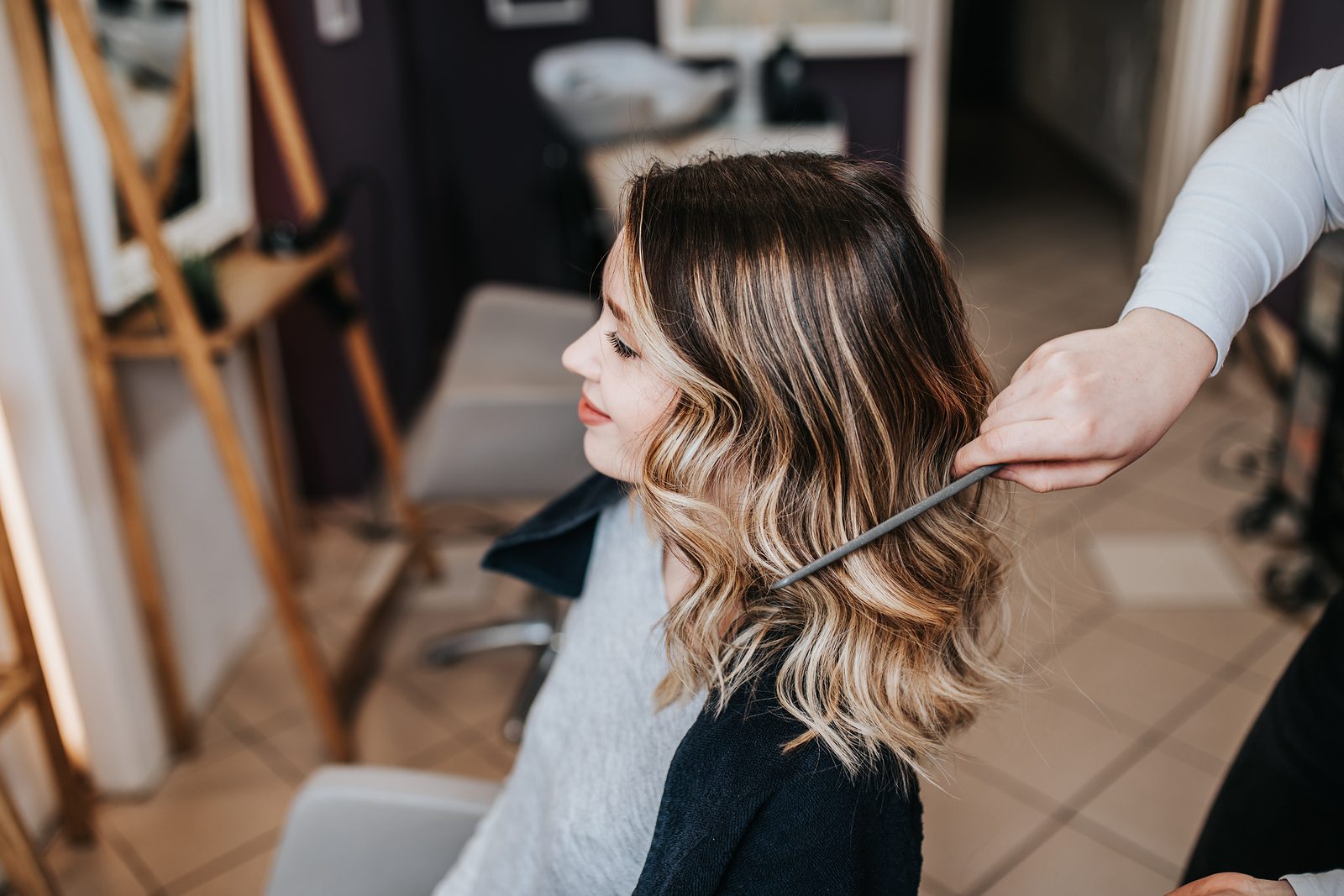 A stylist combs through a client’s long hair with soft, blended brunette-to-blonde balayage in a bright salon.