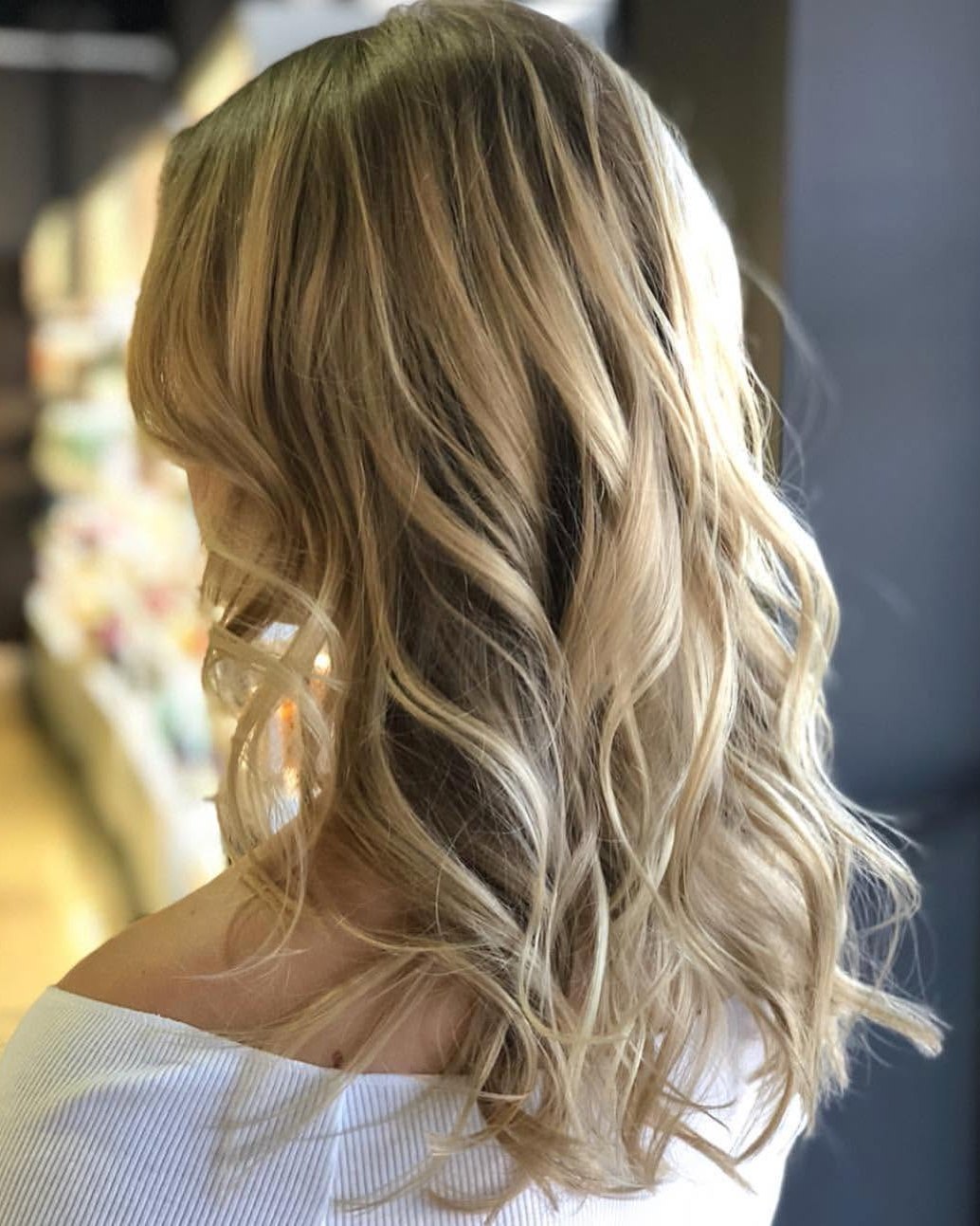 A client's shoulder-length hair from behind, with soft blonde balayage and loose waves