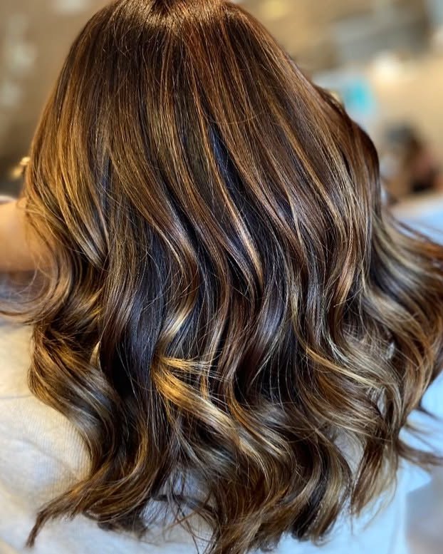 A client's long brunette hair from behind, with caramel and honey balayage in soft waves